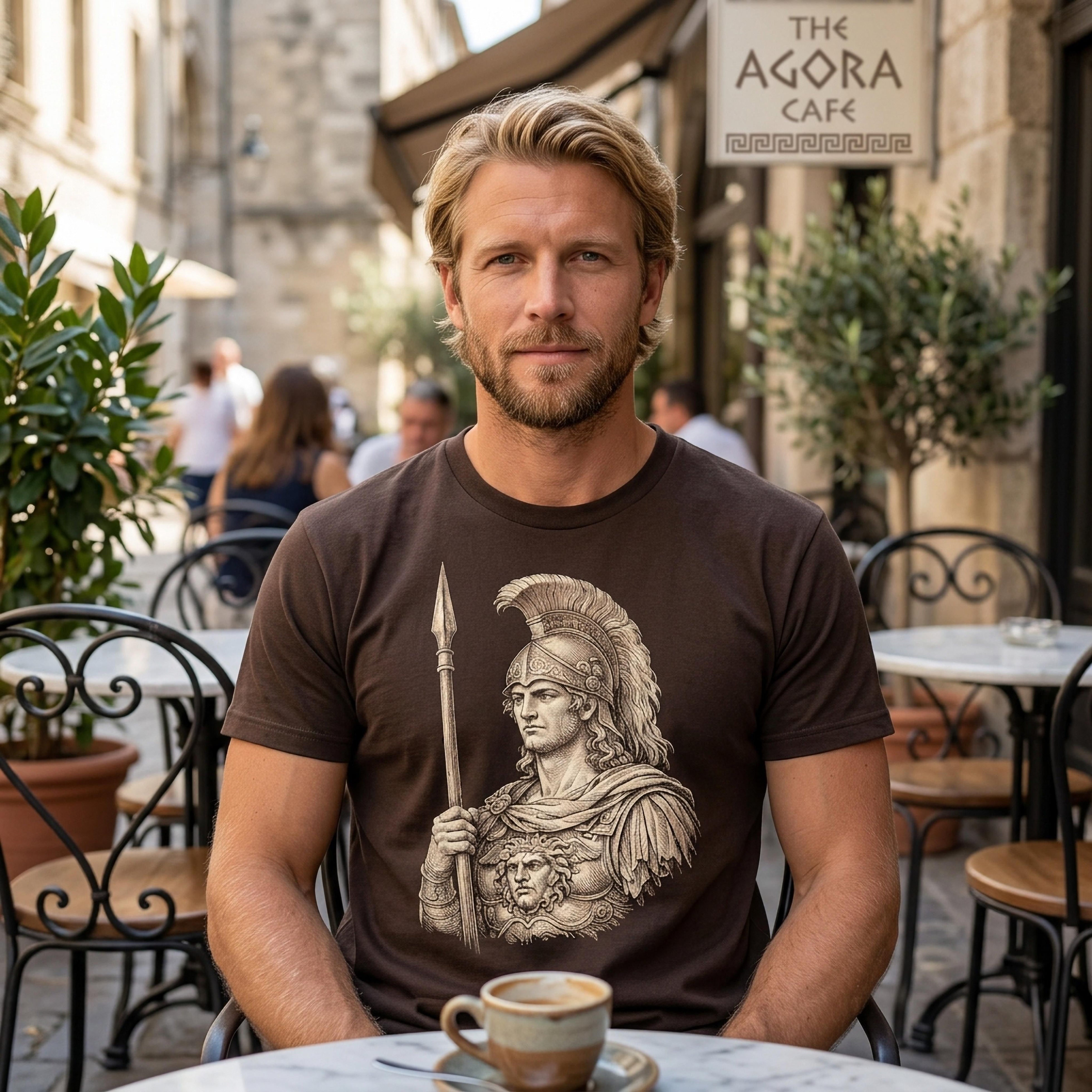 Man in brown t-shirt with ancient warrior graphic sits at cafe table with coffee.