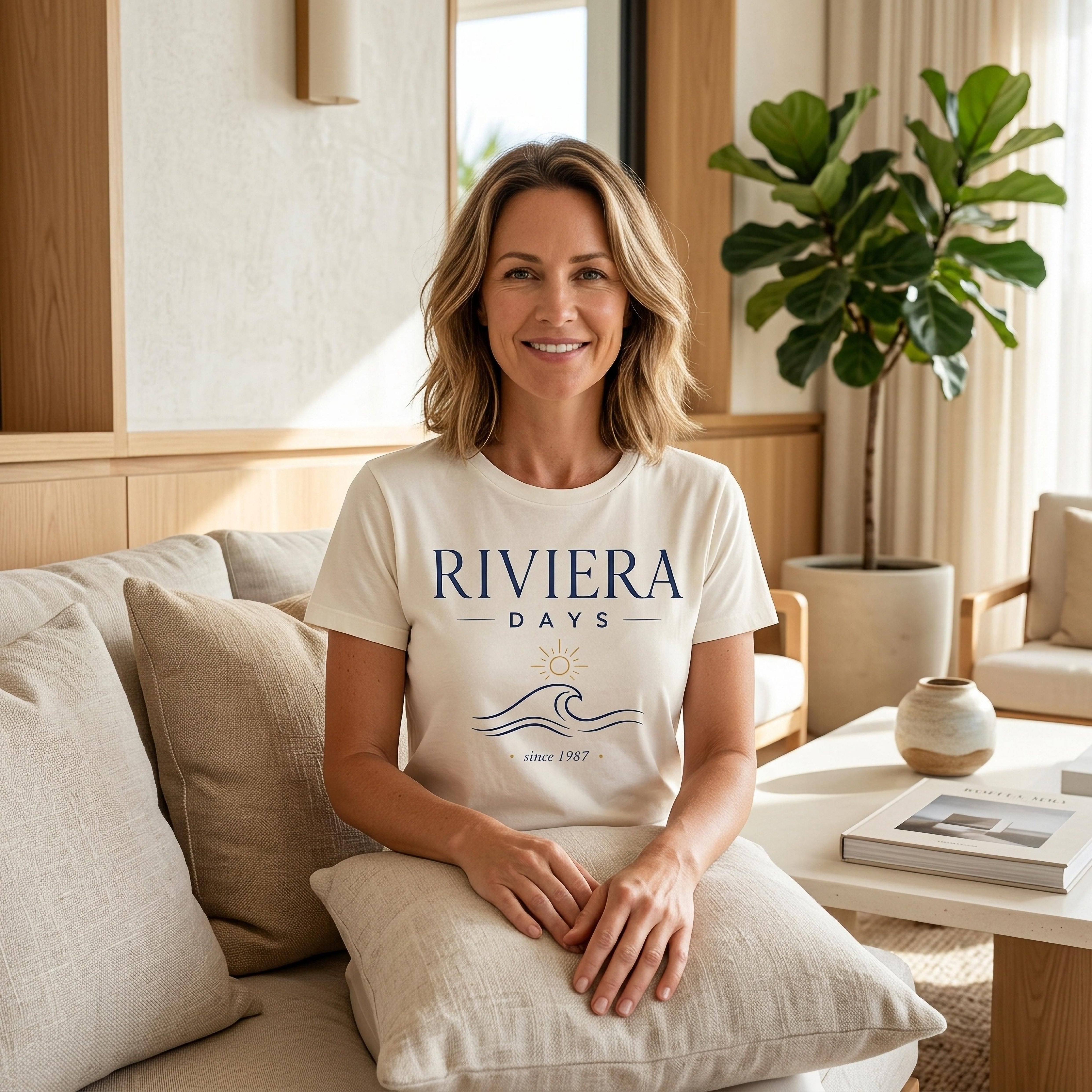 Woman wearing RIVIERA DAYS t-shirt on couch with plant and table.