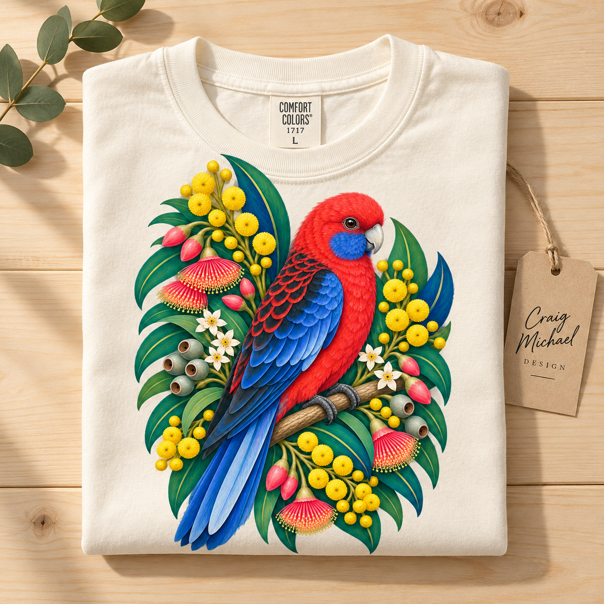 Cream t-shirt with a vibrant red and blue parrot perched among Australian native flora.