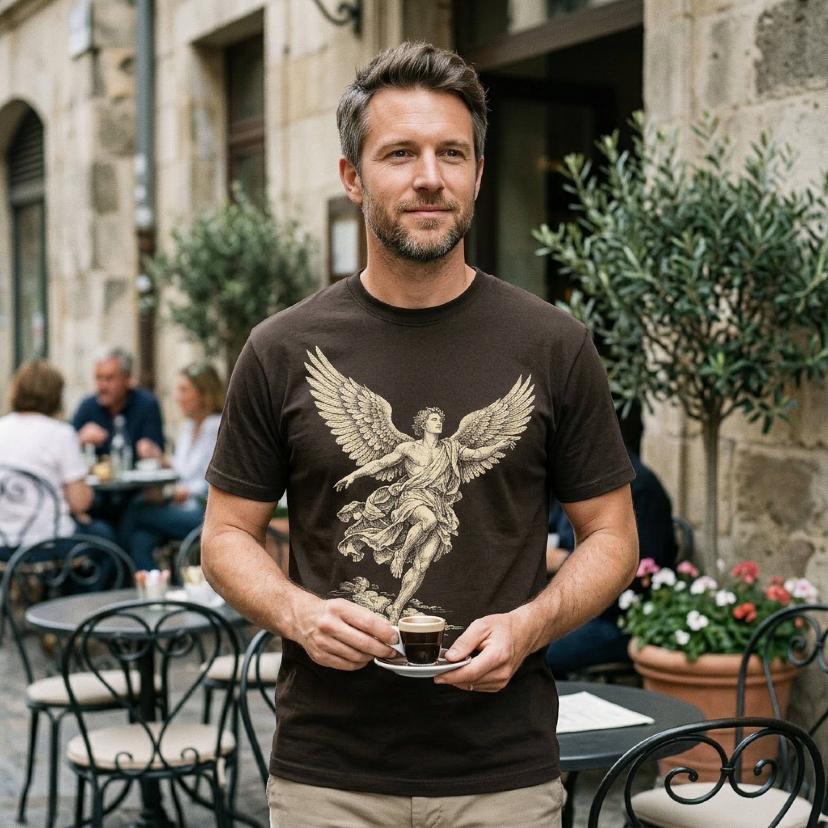 Man in brown t-shirt with winged figure graphic holding a small coffee cup.