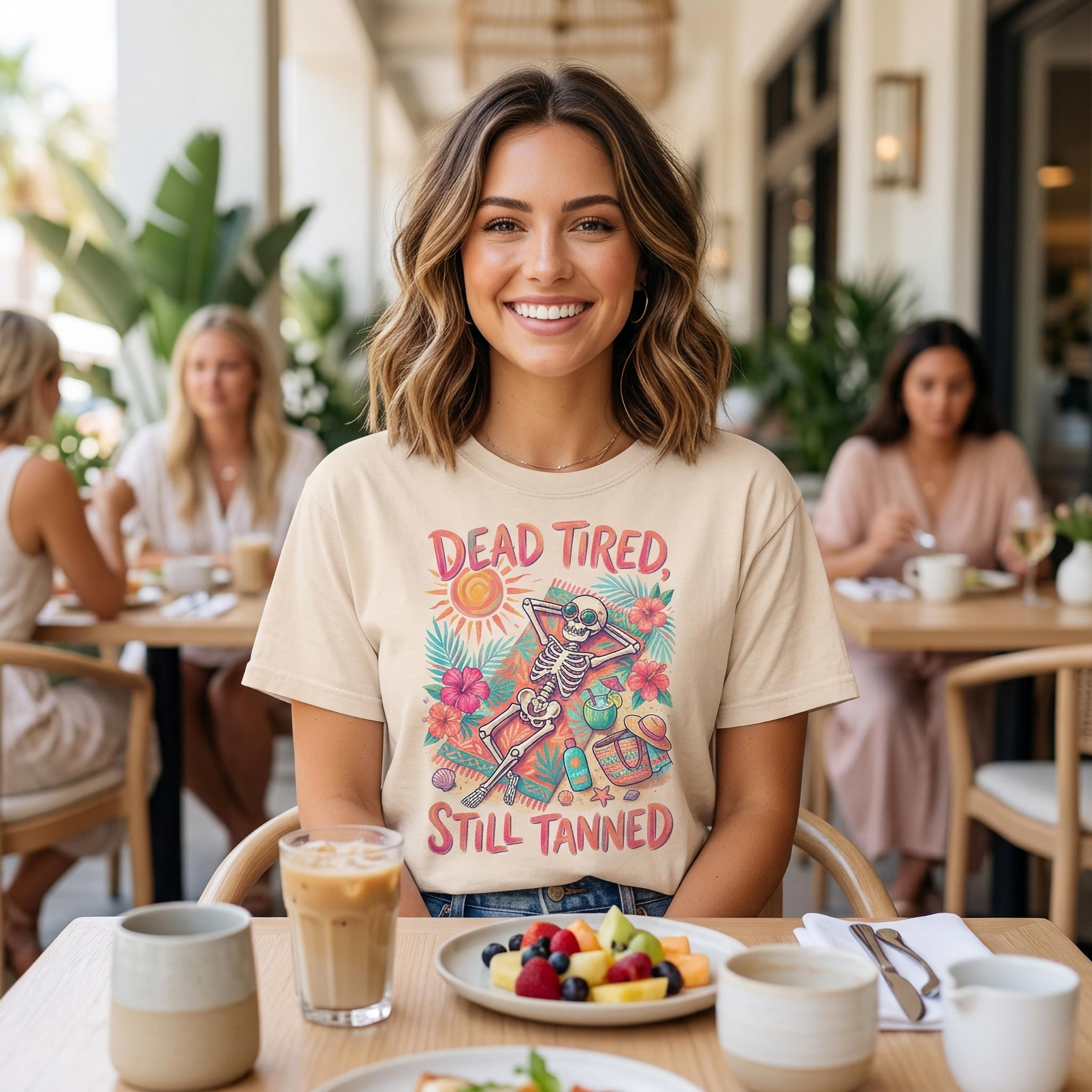 Skeleton graphic t-shirt with text "Dead Tired Still Tanned" featuring tropical elements.