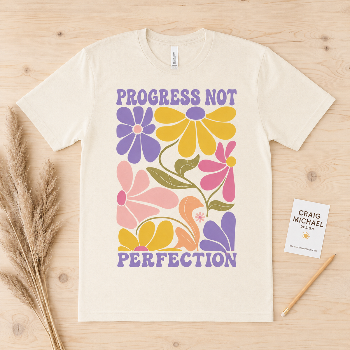Cream t-shirt with "PROGRESS NOT PERFECTION" text and colorful retro flowers.