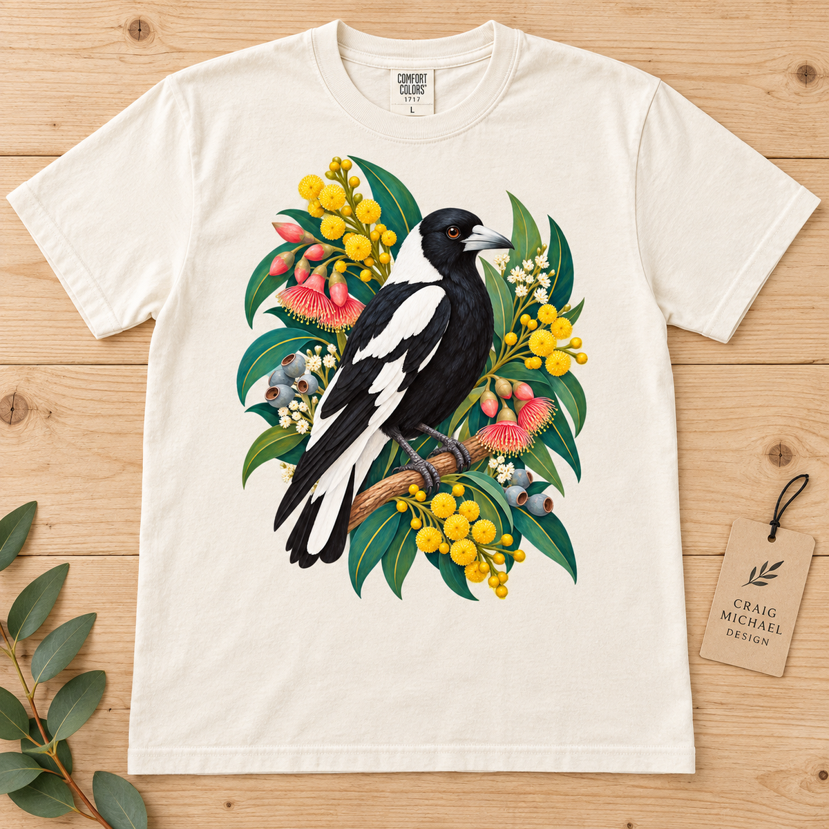 An off-white t-shirt featuring a detailed illustration of an Australian magpie perched on foliage with colorful wildflowers.