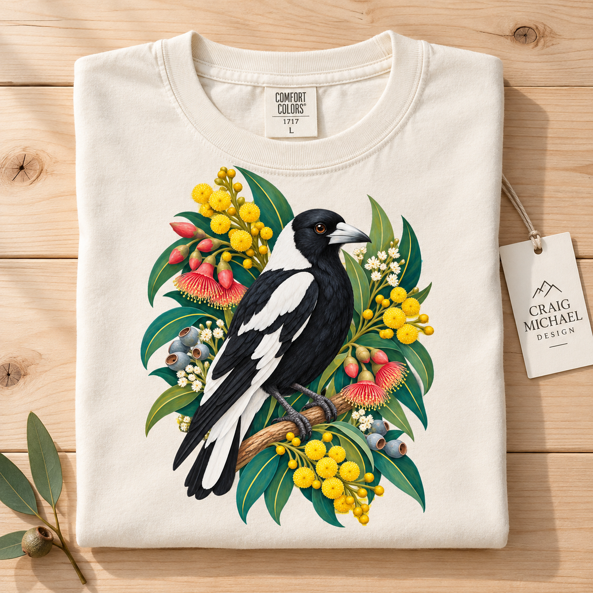 Folded cream t-shirt featuring an illustration of an Australian magpie among colorful native flowers and eucalyptus leaves.