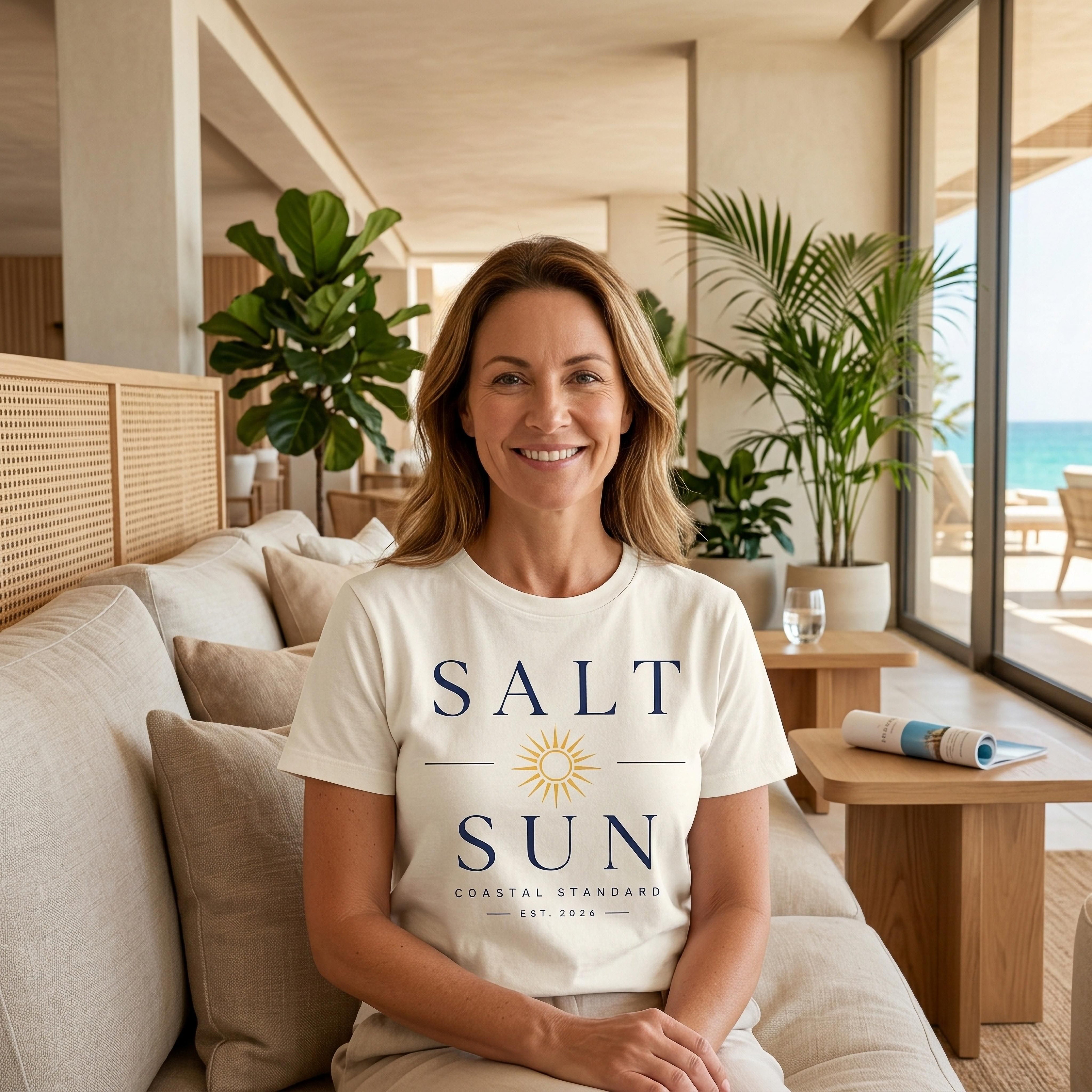 Woman wearing a "Salt & Sun Coastal Standard" t-shirt, seated on a sofa.
