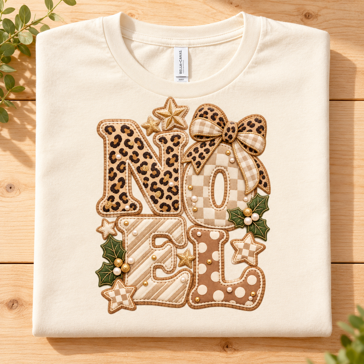 Cream t-shirt with applique letters spelling "NOEL" in festive patterns and embellishments.