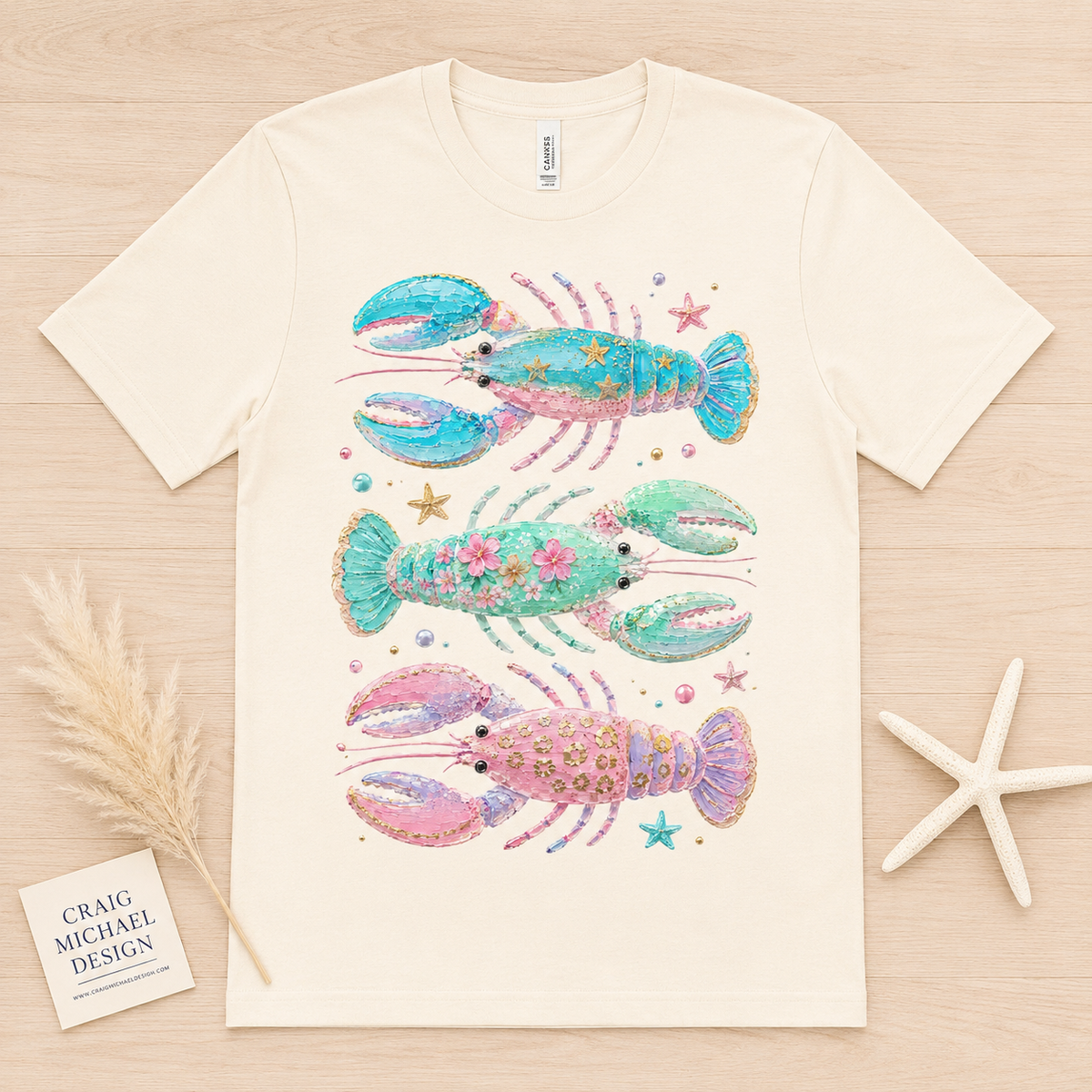 Cream t-shirt with three watercolor lobsters in pink, green, and blue with decorative elements.