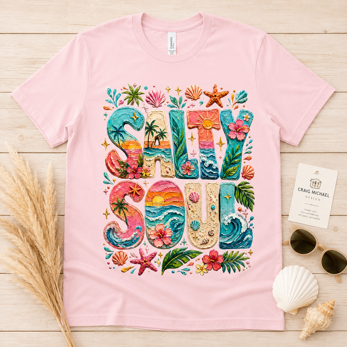 Pink t-shirt with "Salty Soul" in colorful beach-themed lettering and tropical accents.