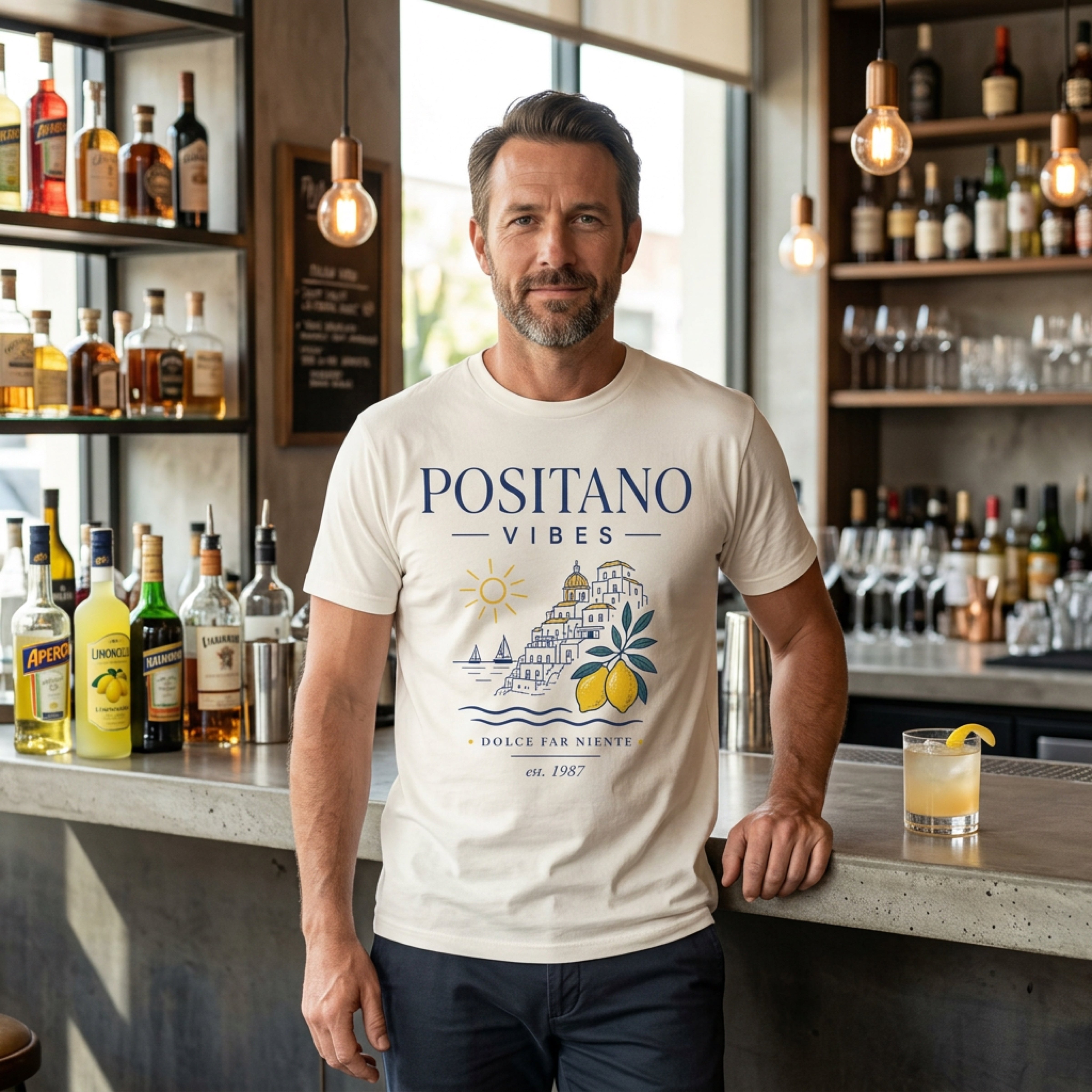 Man wearing a POSITANO VIBES t-shirt standing behind a bar.