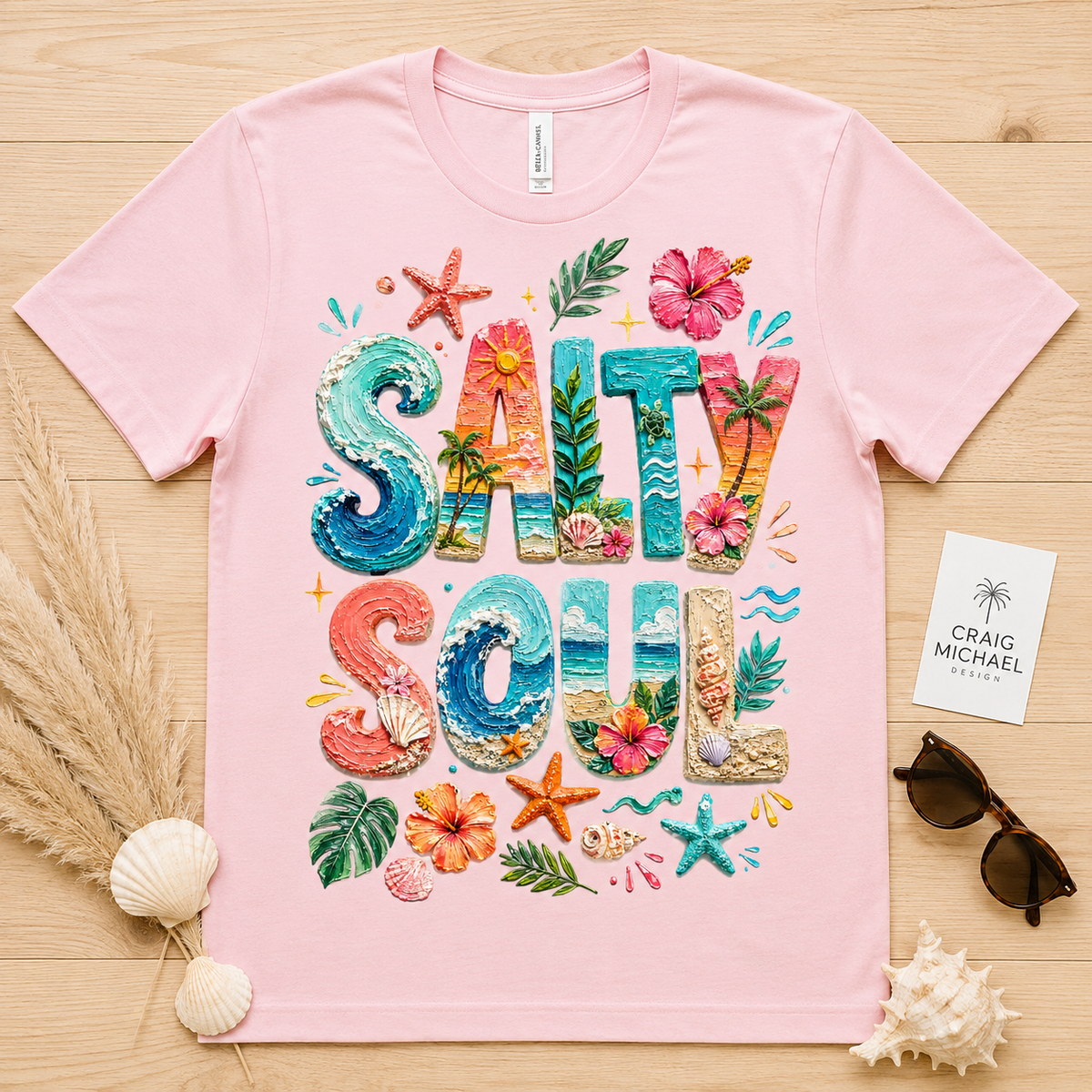 Pink t-shirt with "SALTY SOUL" text design featuring ocean waves, palm trees, and seashells.