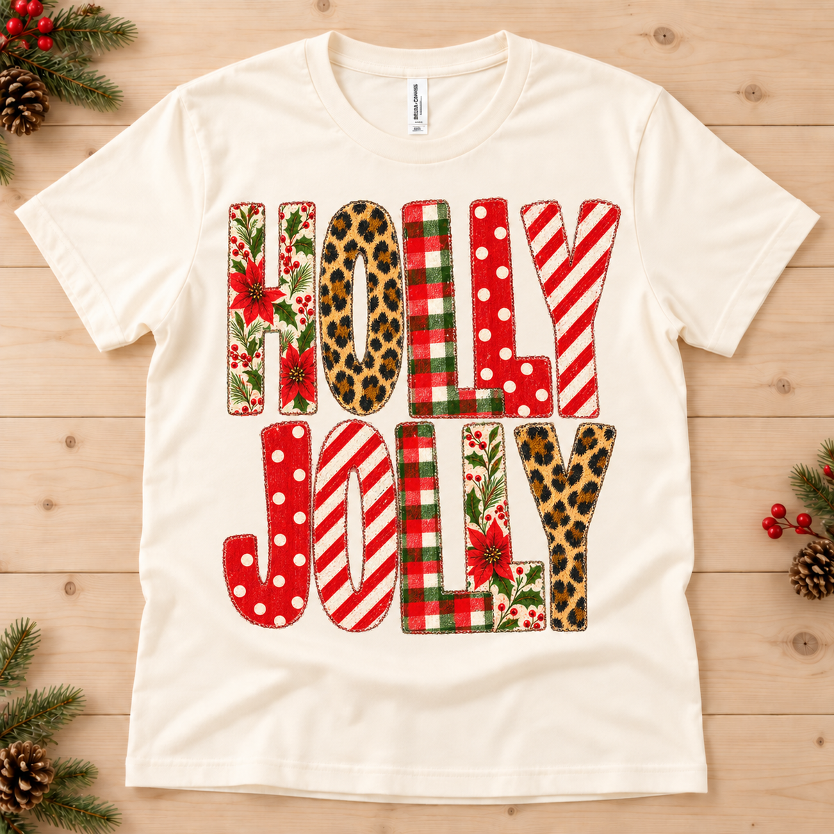 Cream t-shirt with "HOLLY JOLLY" text in festive patterns including poinsettias, leopard print, and buffalo plaid.