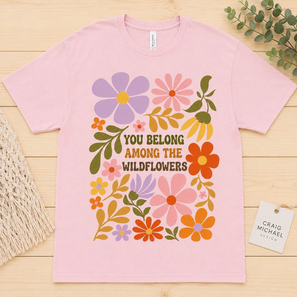 Pink t-shirt with "You Belong Among the Wildflowers" text and colorful floral design.