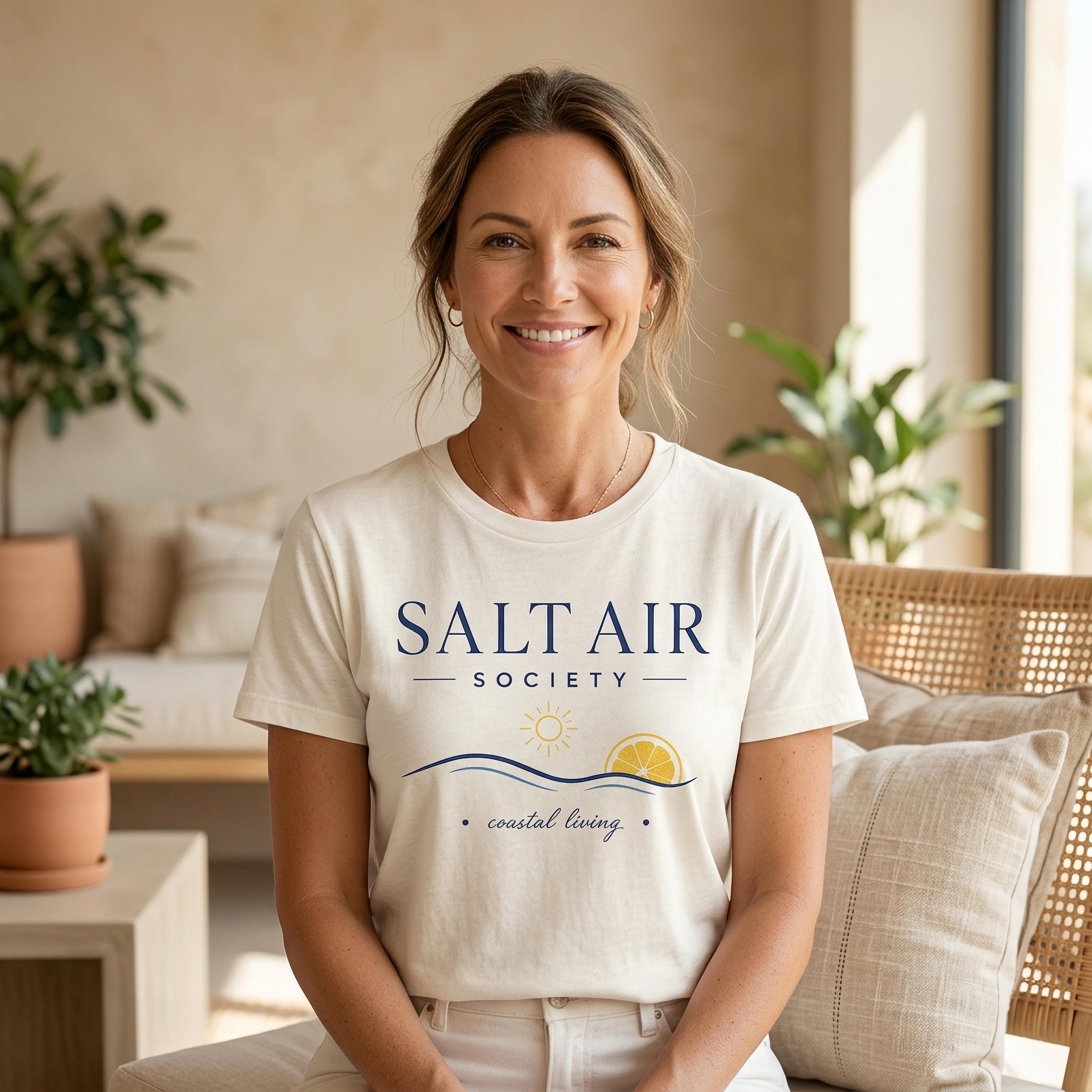Woman wearing a cream t-shirt with "Salt Air Society" and a lemon sun logo.