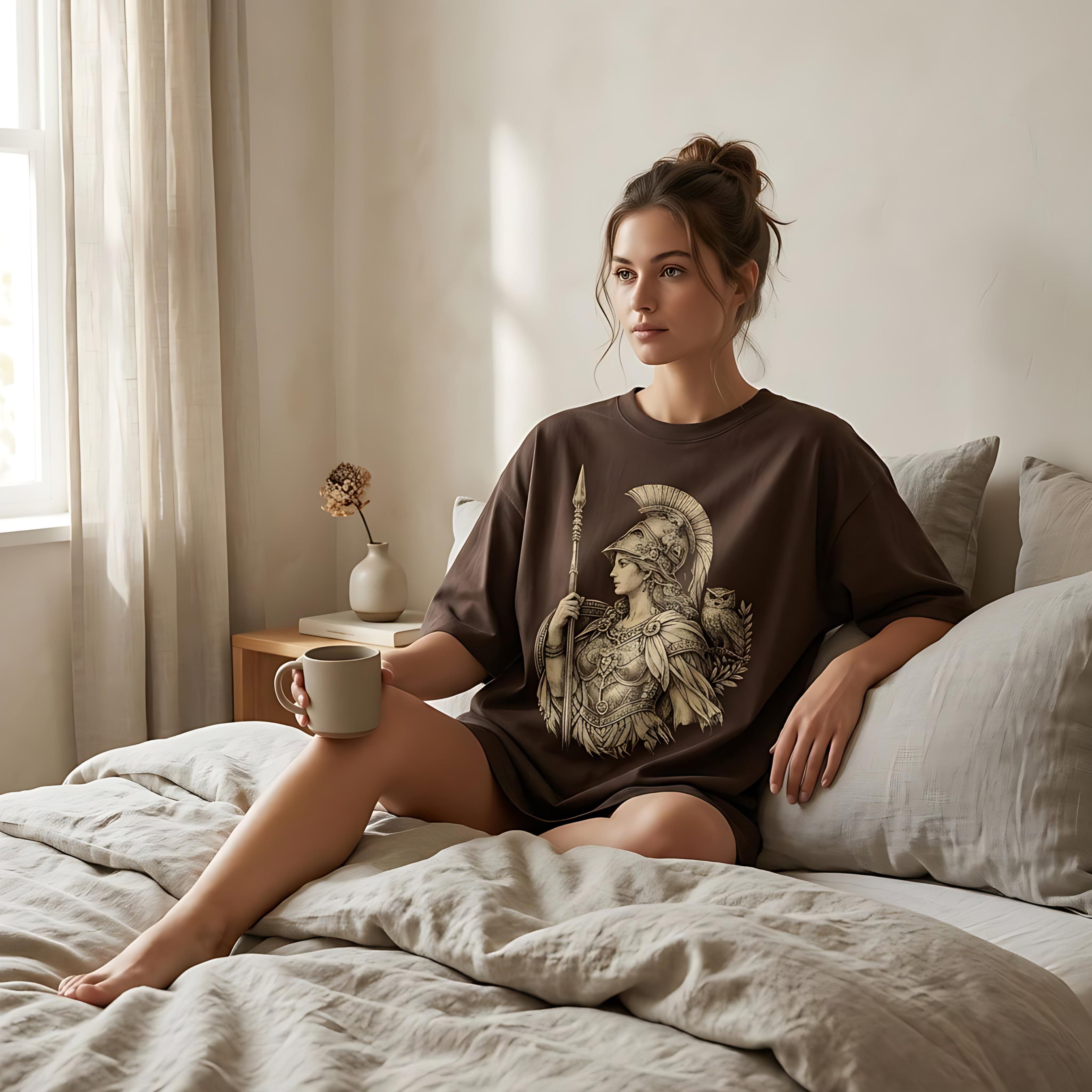 Woman in a brown t-shirt featuring a Spartan warrior graphic, sitting on a bed.