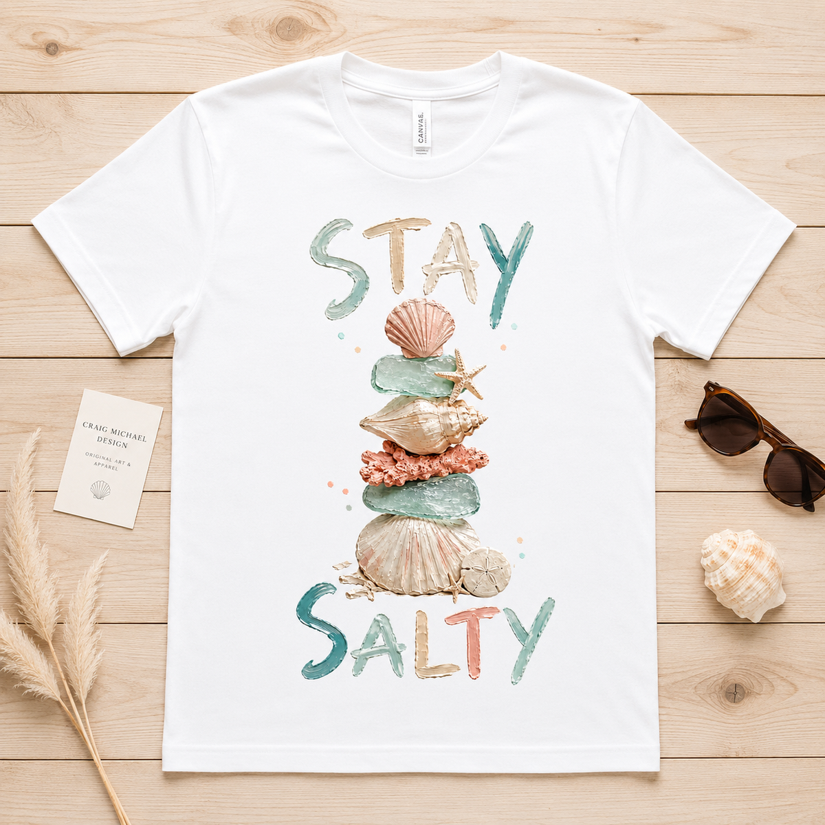 White t-shirt with "STAY SALTY" text and stacked seashells and sea glass.