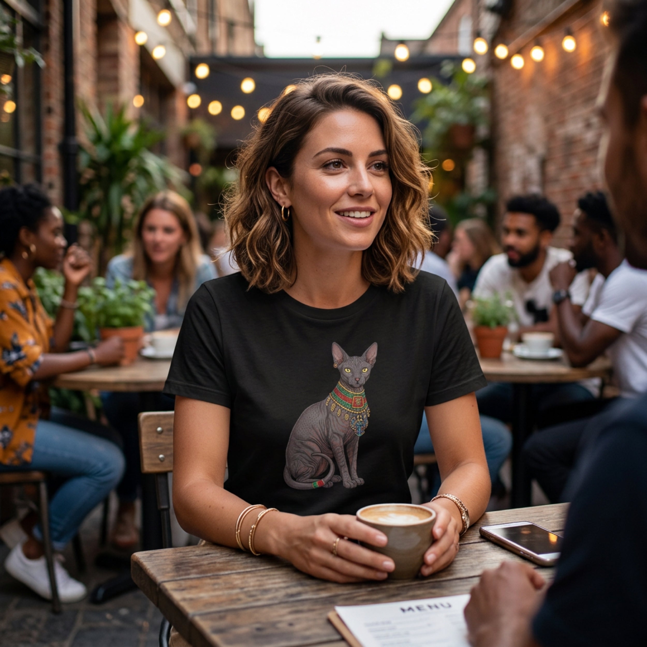 Woman wearing a black t-shirt with a Sphynx cat graphic holding a coffee cup.