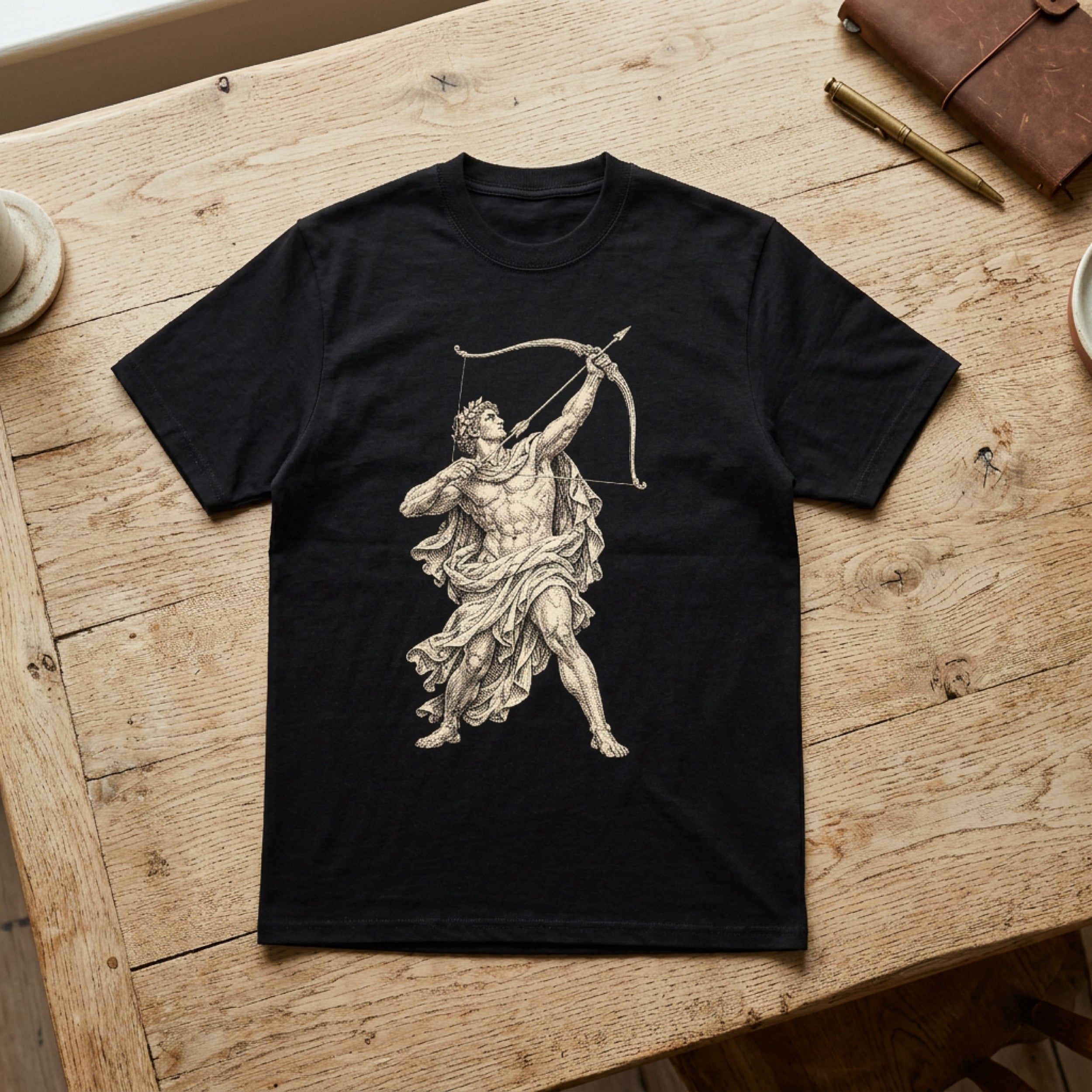 Black t-shirt with Apollo drawing a bow, on a wooden table.