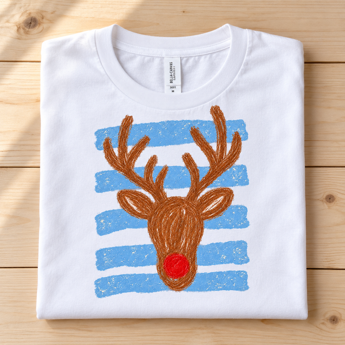White t-shirt with a cartoon reindeer graphic featuring a red nose and blue stripes.