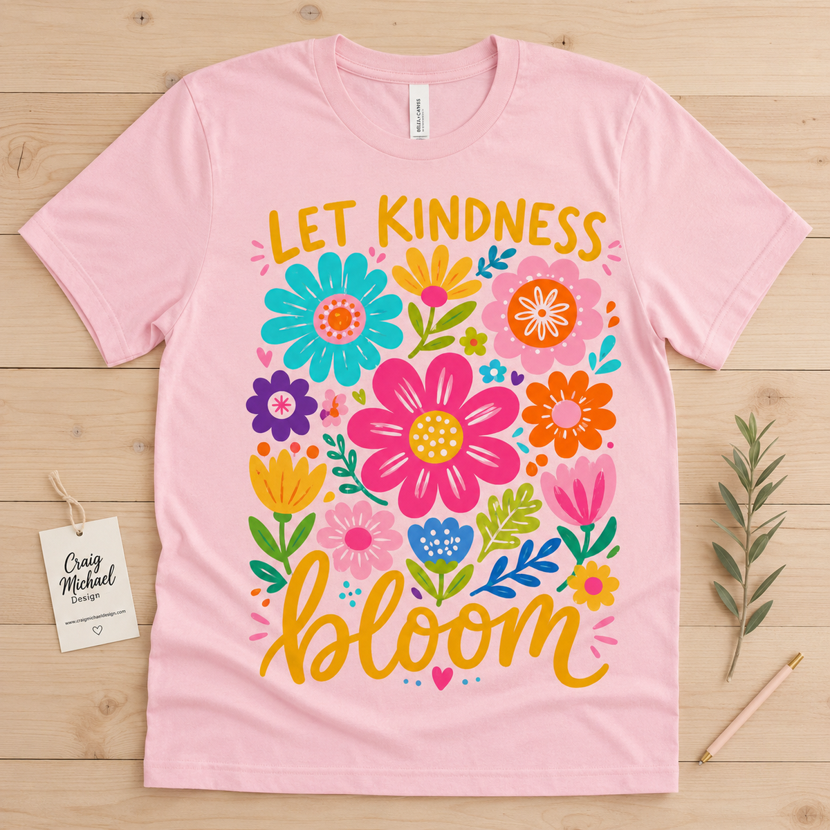 Pink t-shirt with colorful floral design and text "LET KINDNESS bloom".