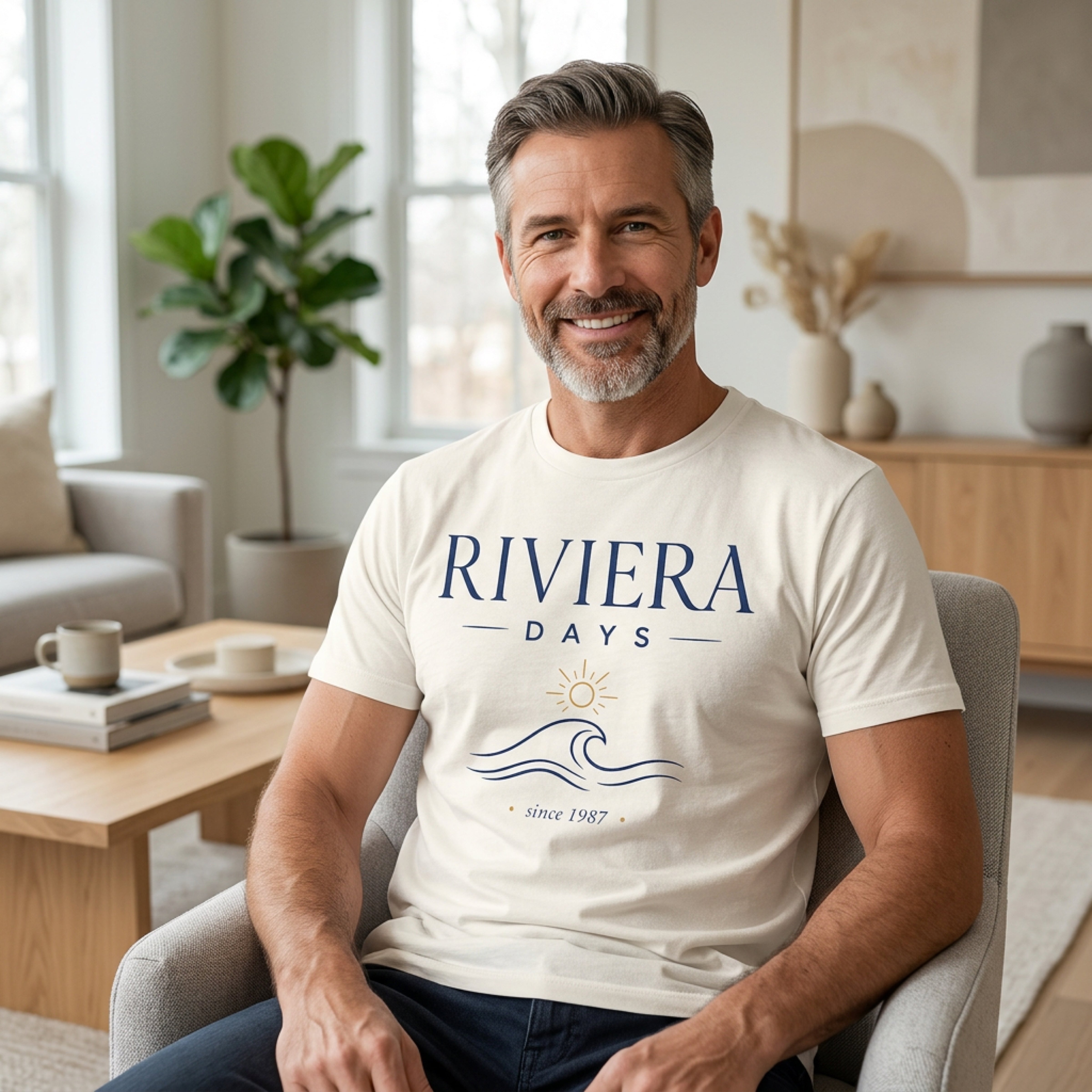 Man in cream t-shirt with "Riviera Days Since 1987" logo sits in chair.