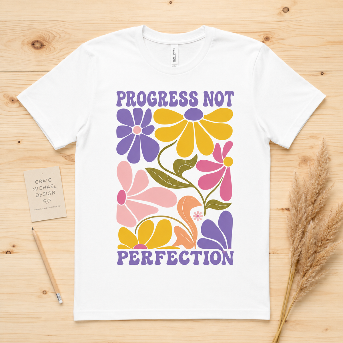 White t-shirt with "Progress Not Perfection" text and colorful floral design.
