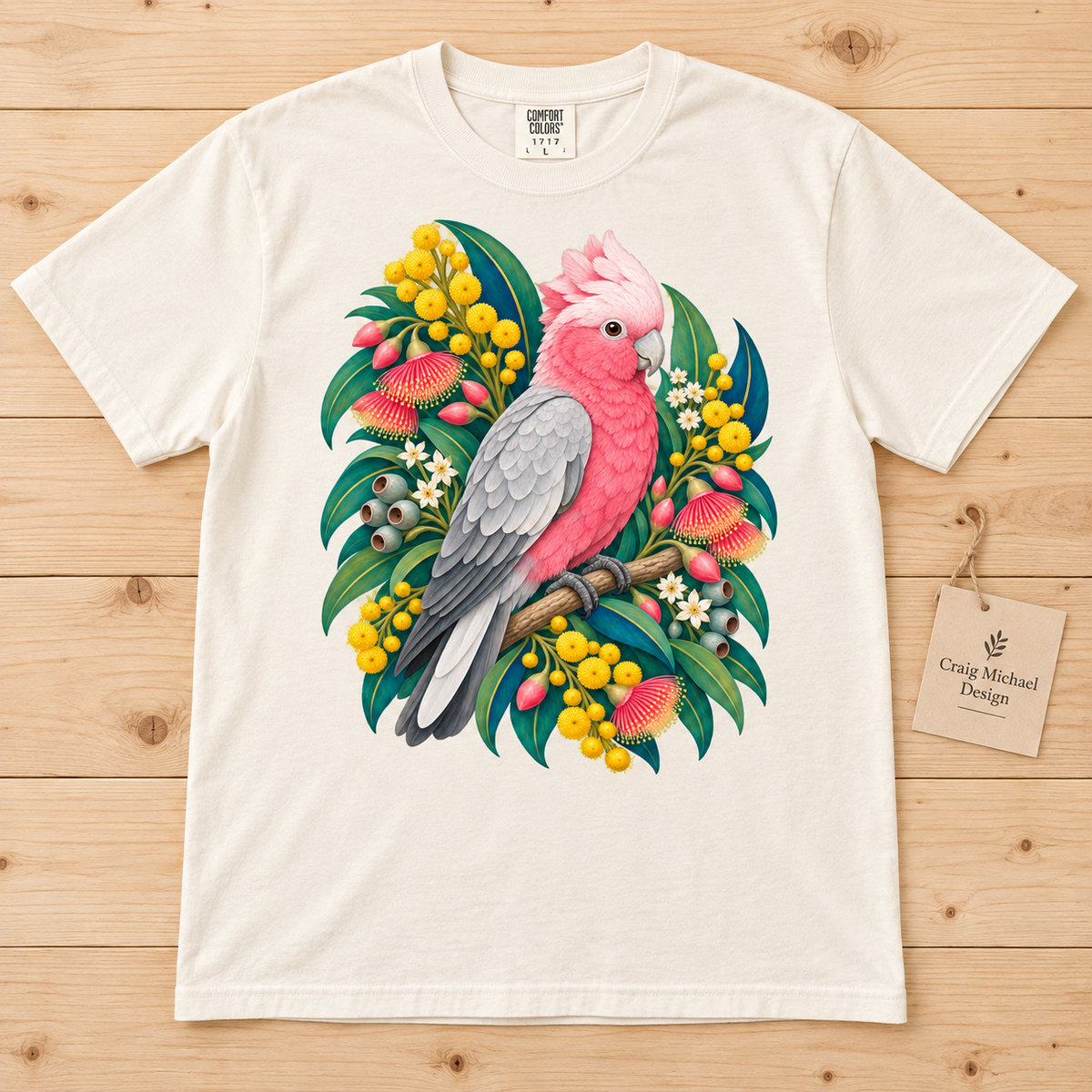 T-shirt with pink and grey cockatoo perched on a branch surrounded by Australian native flowers and foliage.
