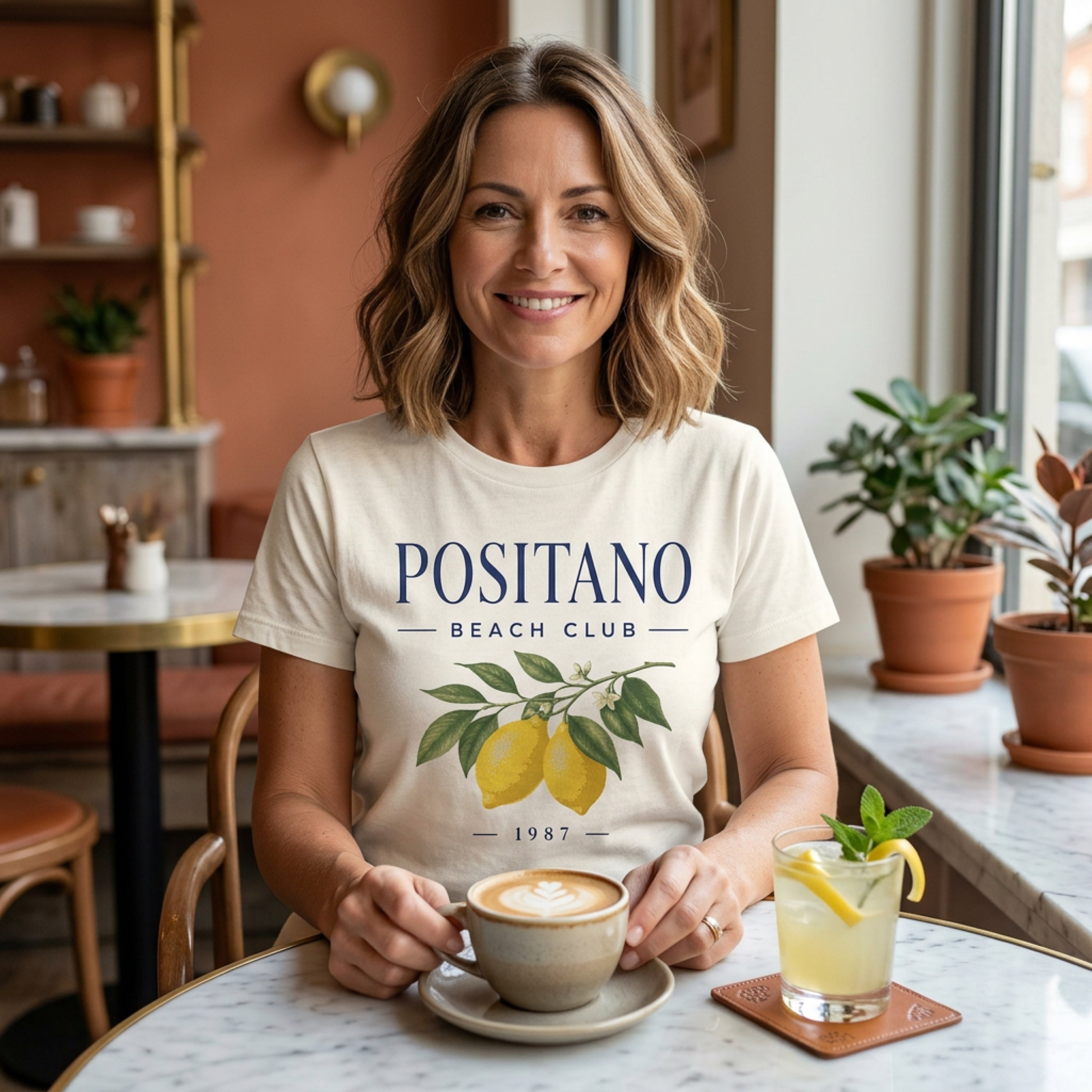 Woman wearing a cream t-shirt with "Positano Beach Club" and lemon graphic.