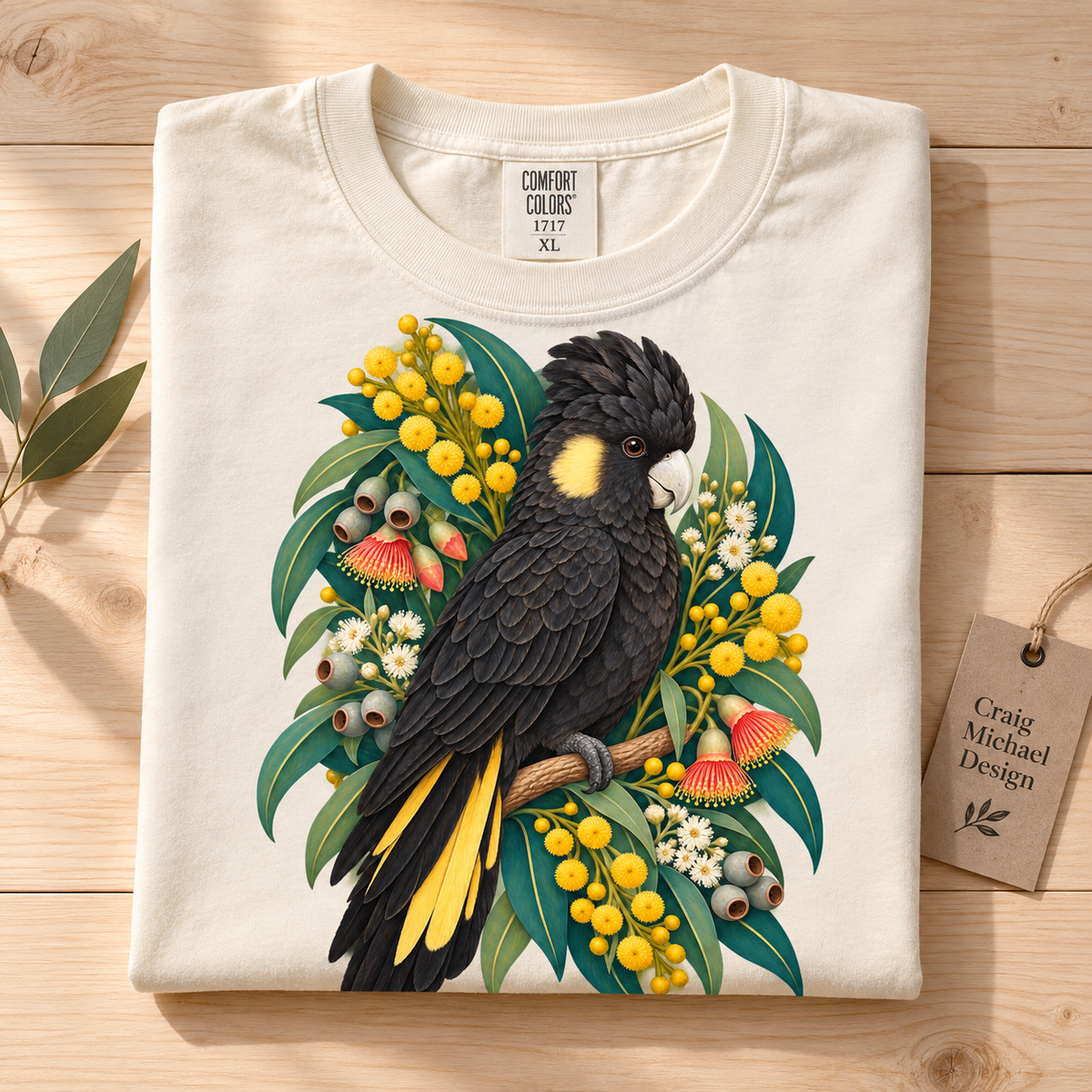 T-shirt with a black cockatoo perched among yellow wattle flowers and eucalyptus leaves.